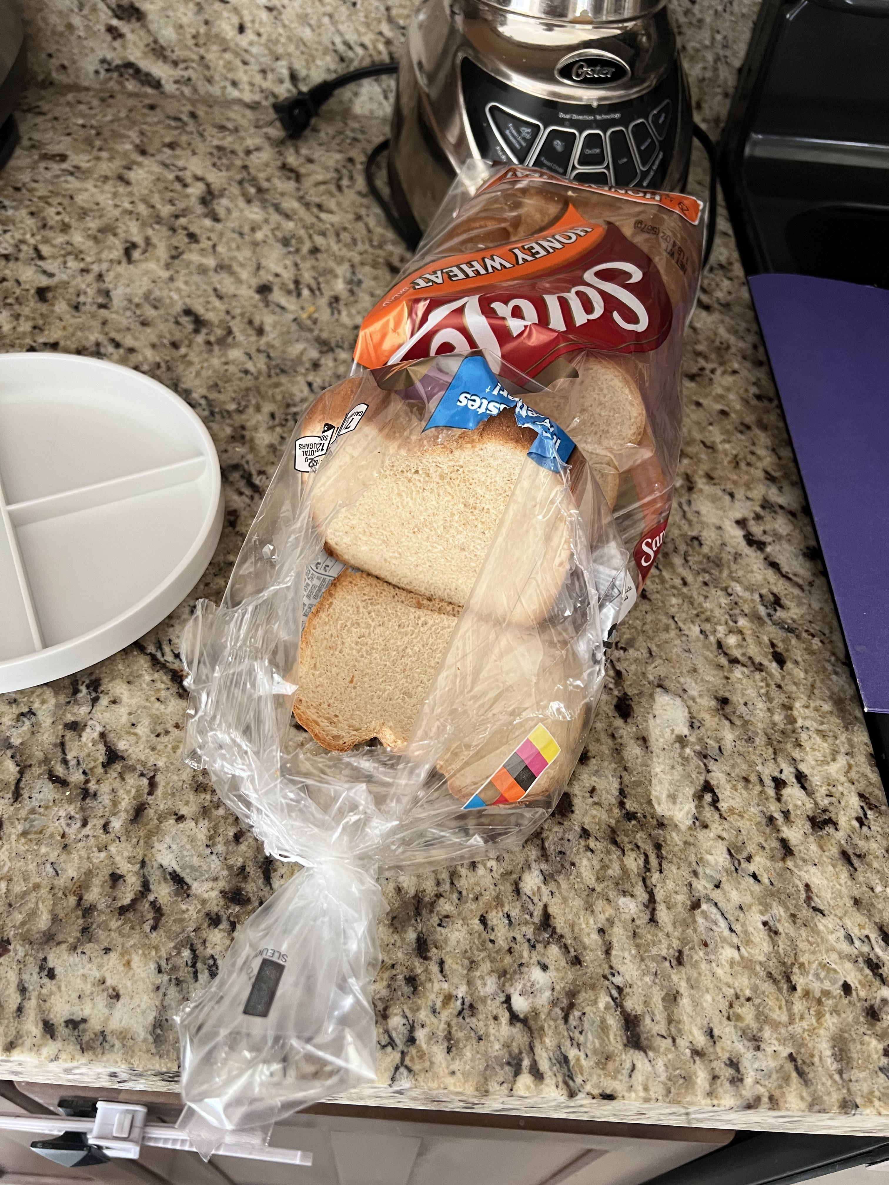 A loaf of bread partially out of its bag on a kitchen counter beside a toaster