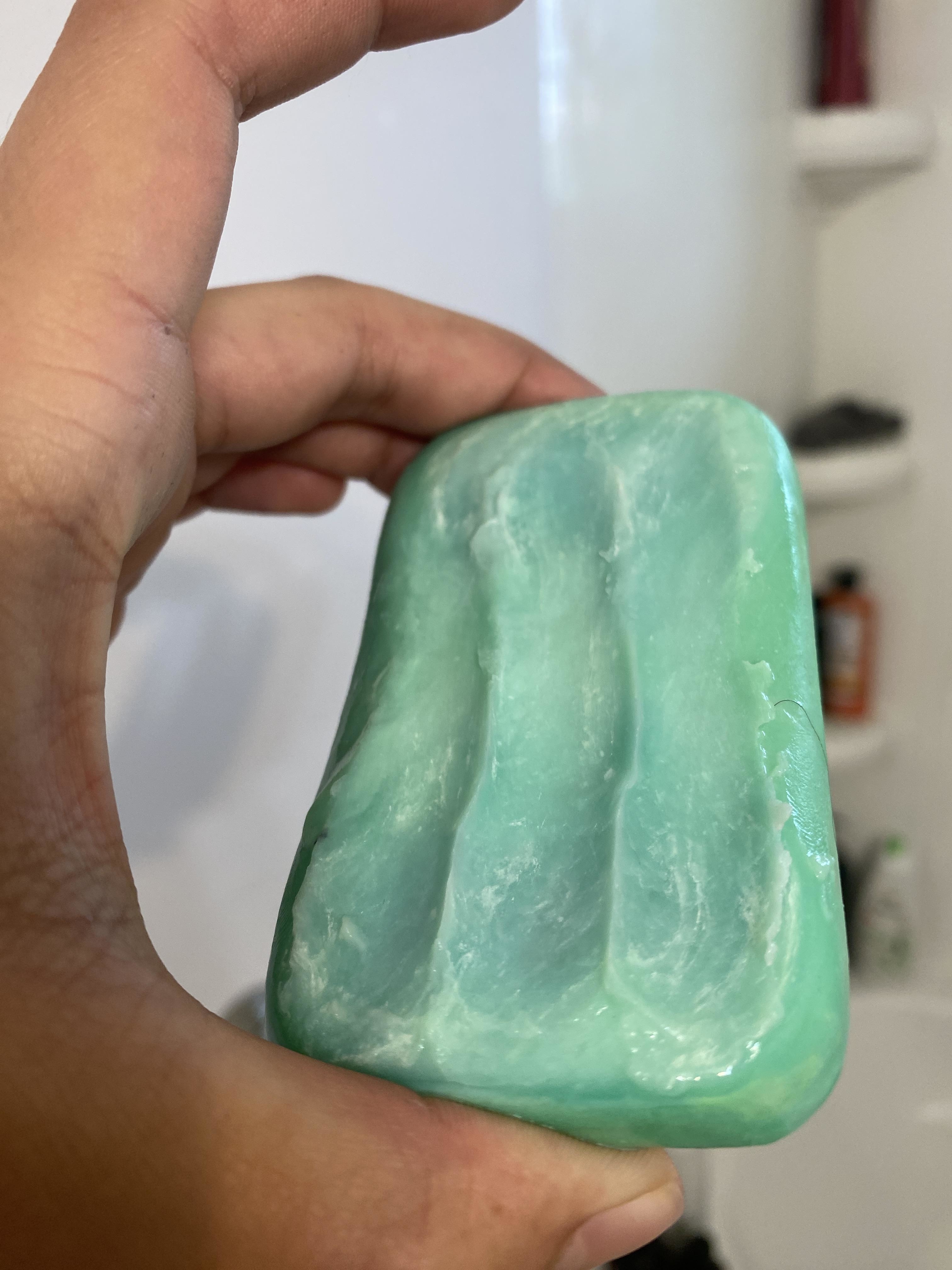 Hand holding a partially used bar of green soap with a bathroom background