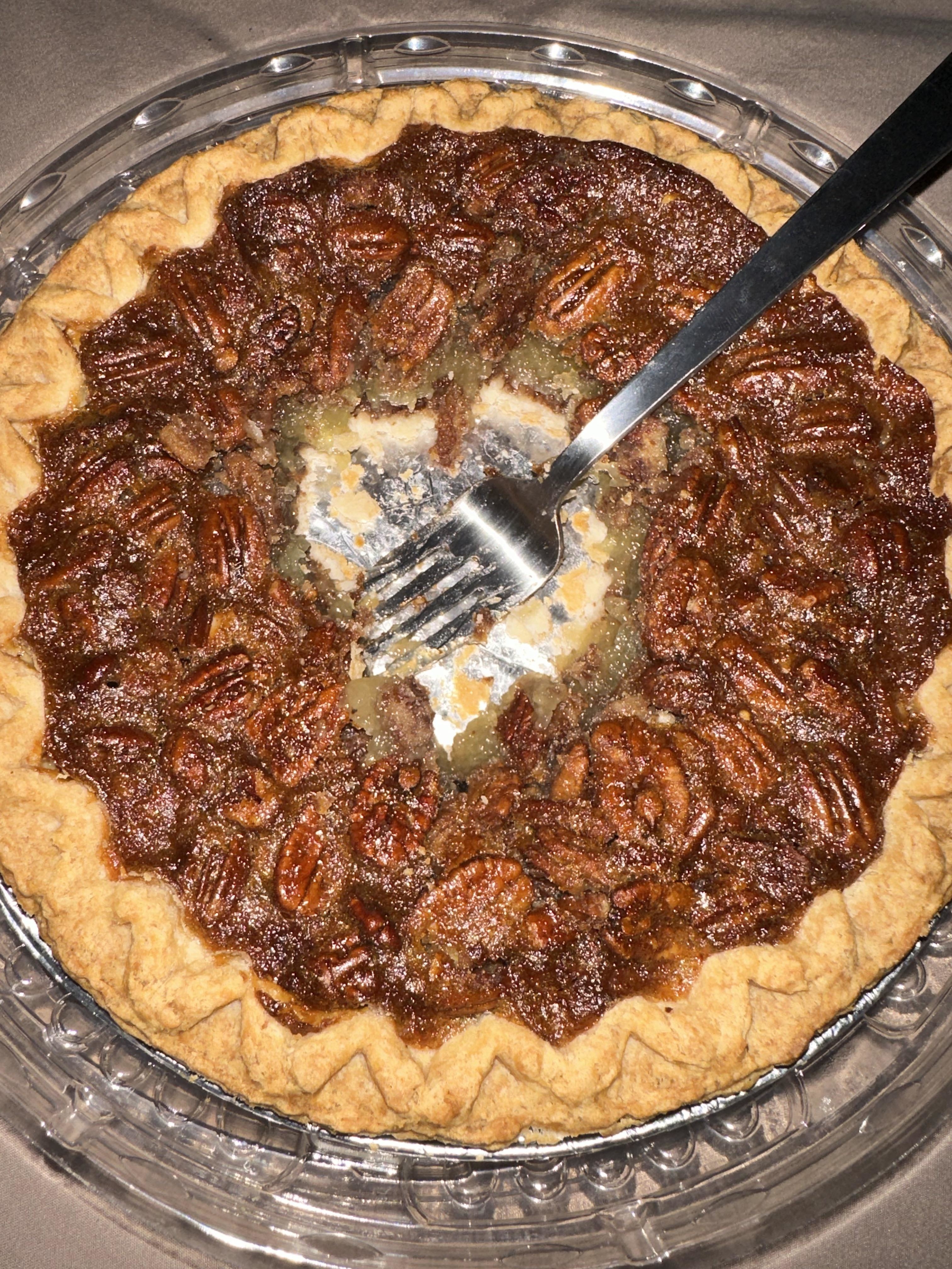 A freshly baked pecan pie with a slice missing, served in a clear pie container
