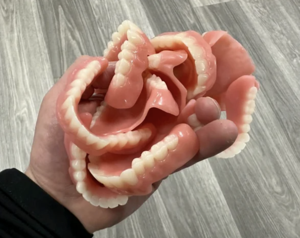 A hand holding a creatively folded dentures sculpture, resembling a fabric piece