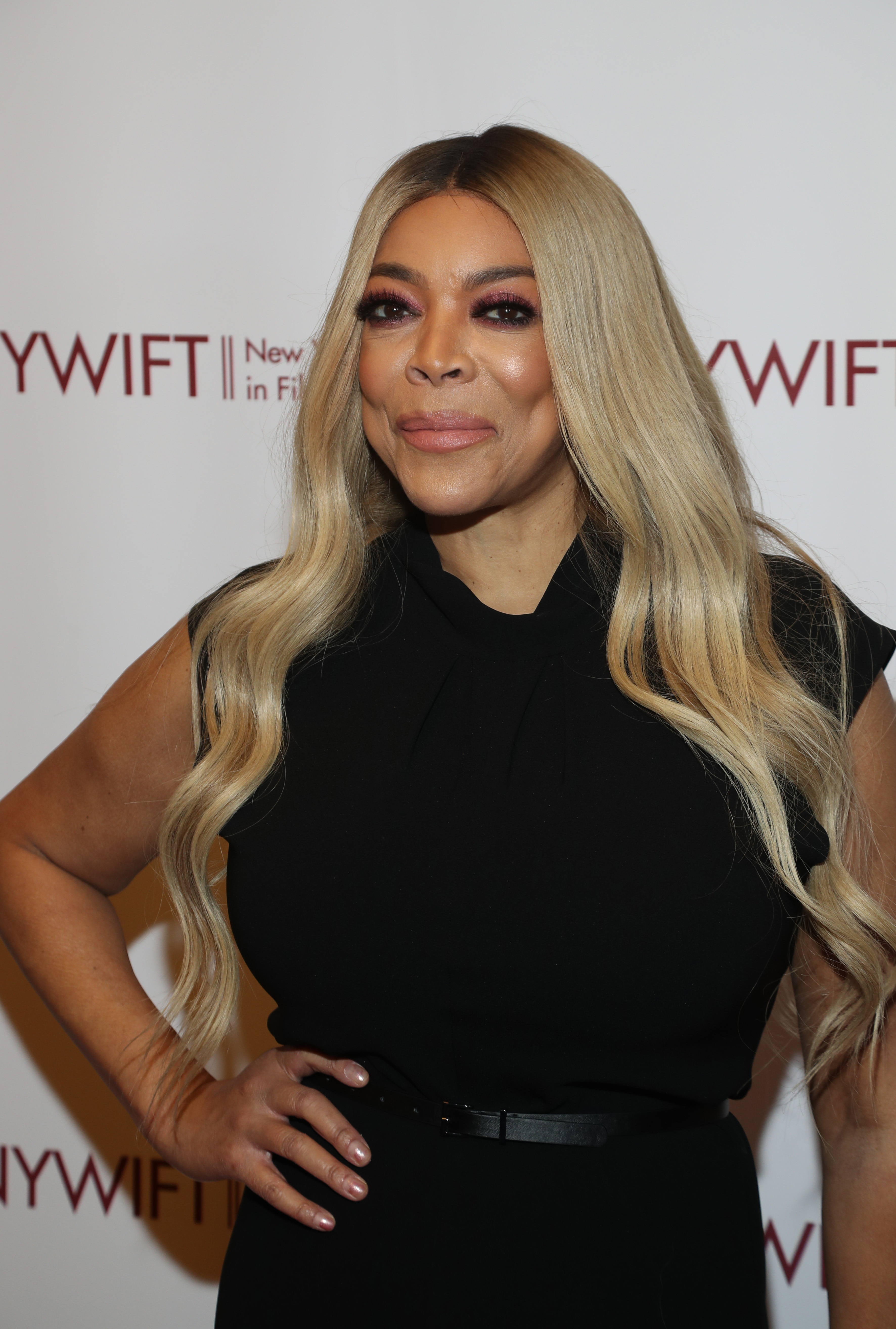 Wendy Williams stands posing in a sleeveless dress with a belt at an event