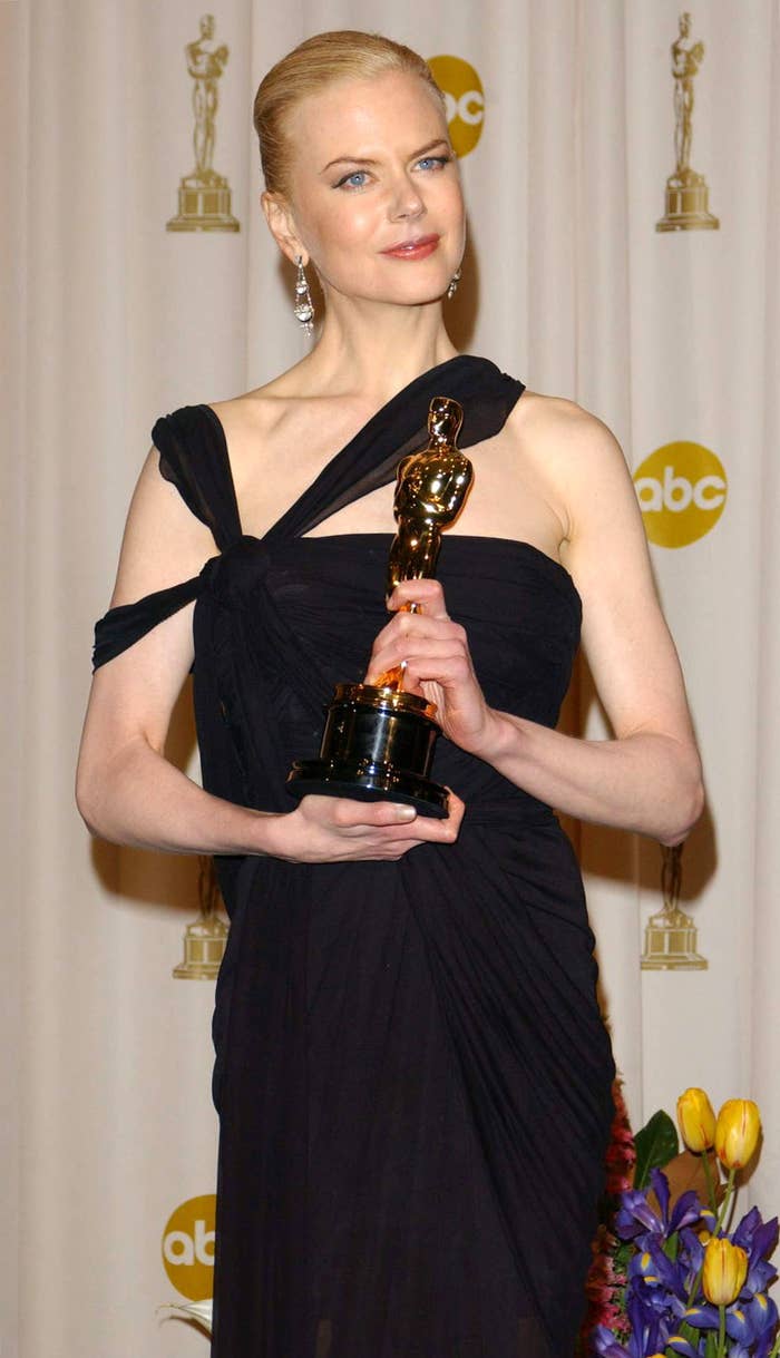 Nicole Kidman in a black, one-shoulder dress holding an Oscar trophy