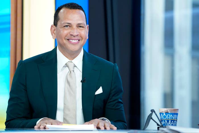 Alex Rodriguez in a suit, sitting at a desk with a &quot;Morning Joe&quot; mug, smiling