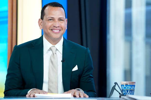 Alex Rodriguez in a suit, sitting at a desk with a "Morning Joe" mug, smiling