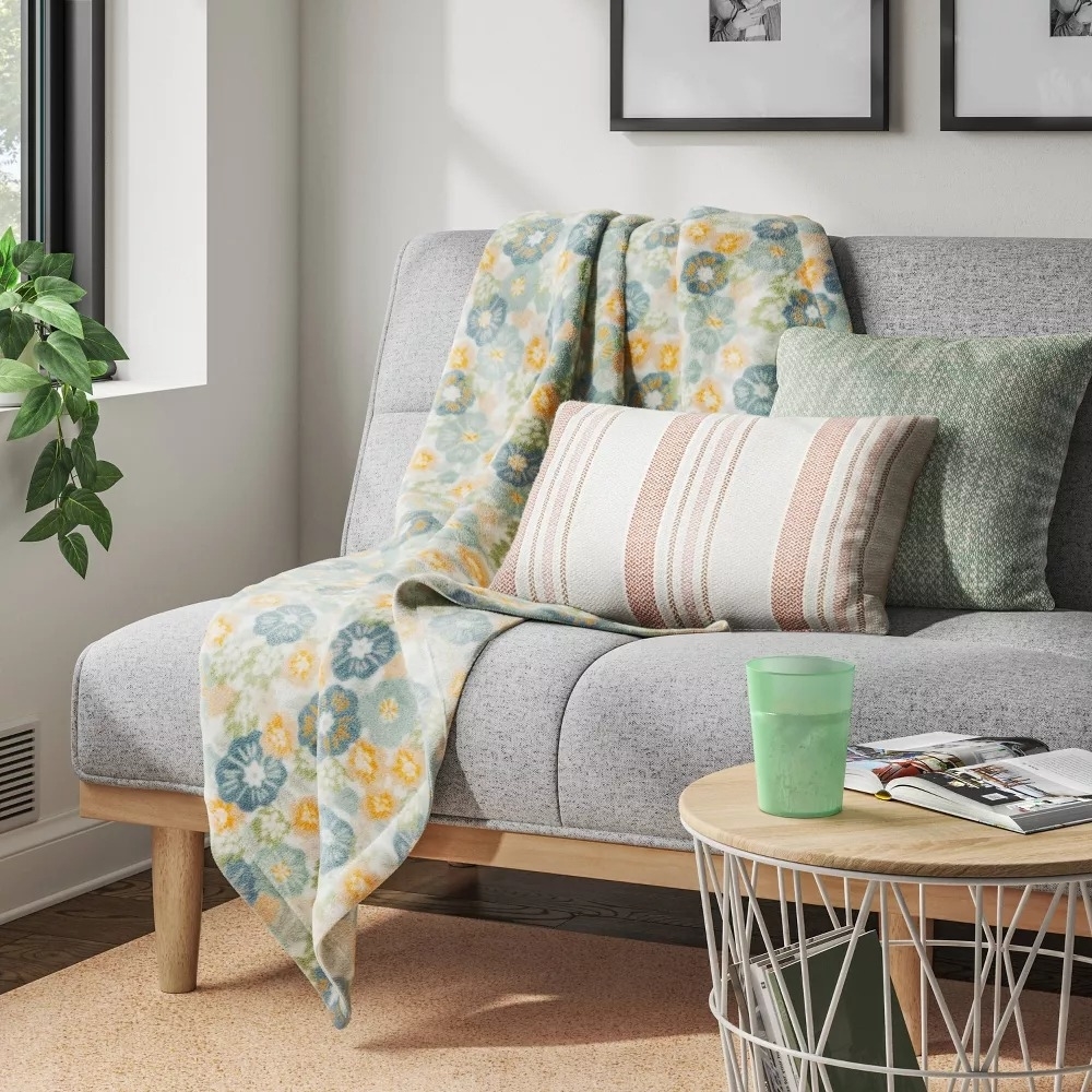 A cozy living room scene with a grey sofa adorned with patterned throw and striped cushion, a round coffee table with a cup and magazine