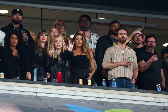 Group of people watching intently from a stadium box office; some pointing and gesturing. Names cannot be provided