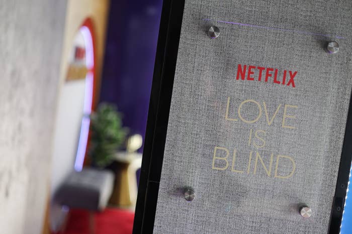 Text on a board reads &quot;NETFLIX LOVE IS BLIND&quot; with blurred background