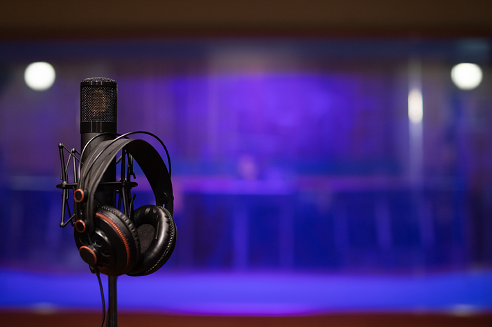 Studio microphone with headphones hanging on it, background blurred with purple hue. No persons visible