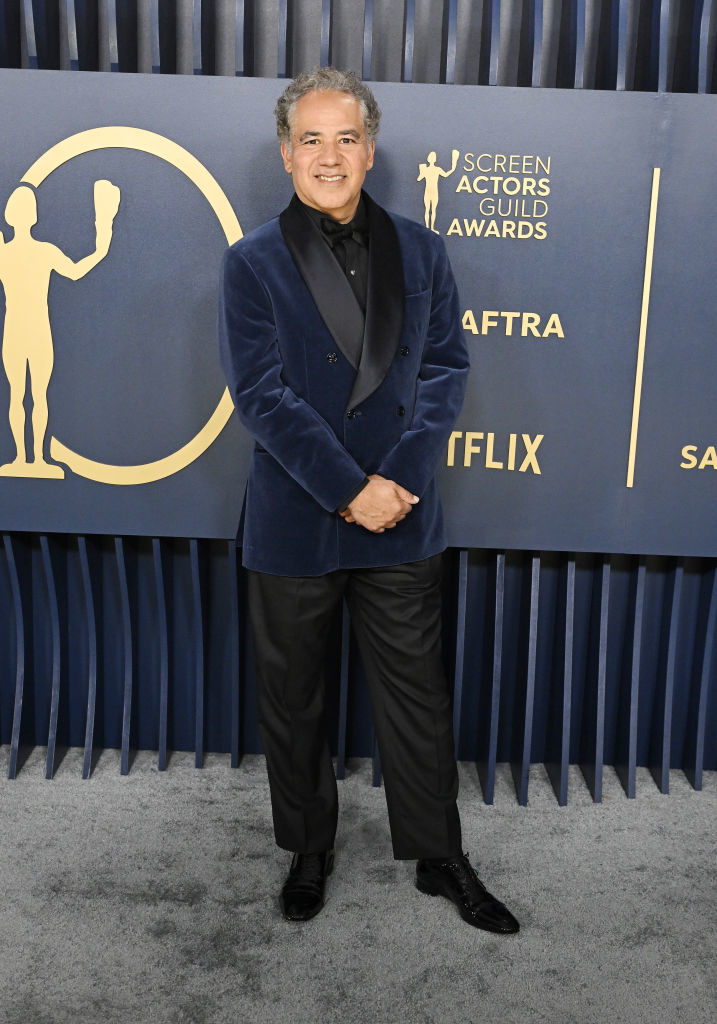 John Ortiz  stands smiling in a formal velvet jacket suit pants