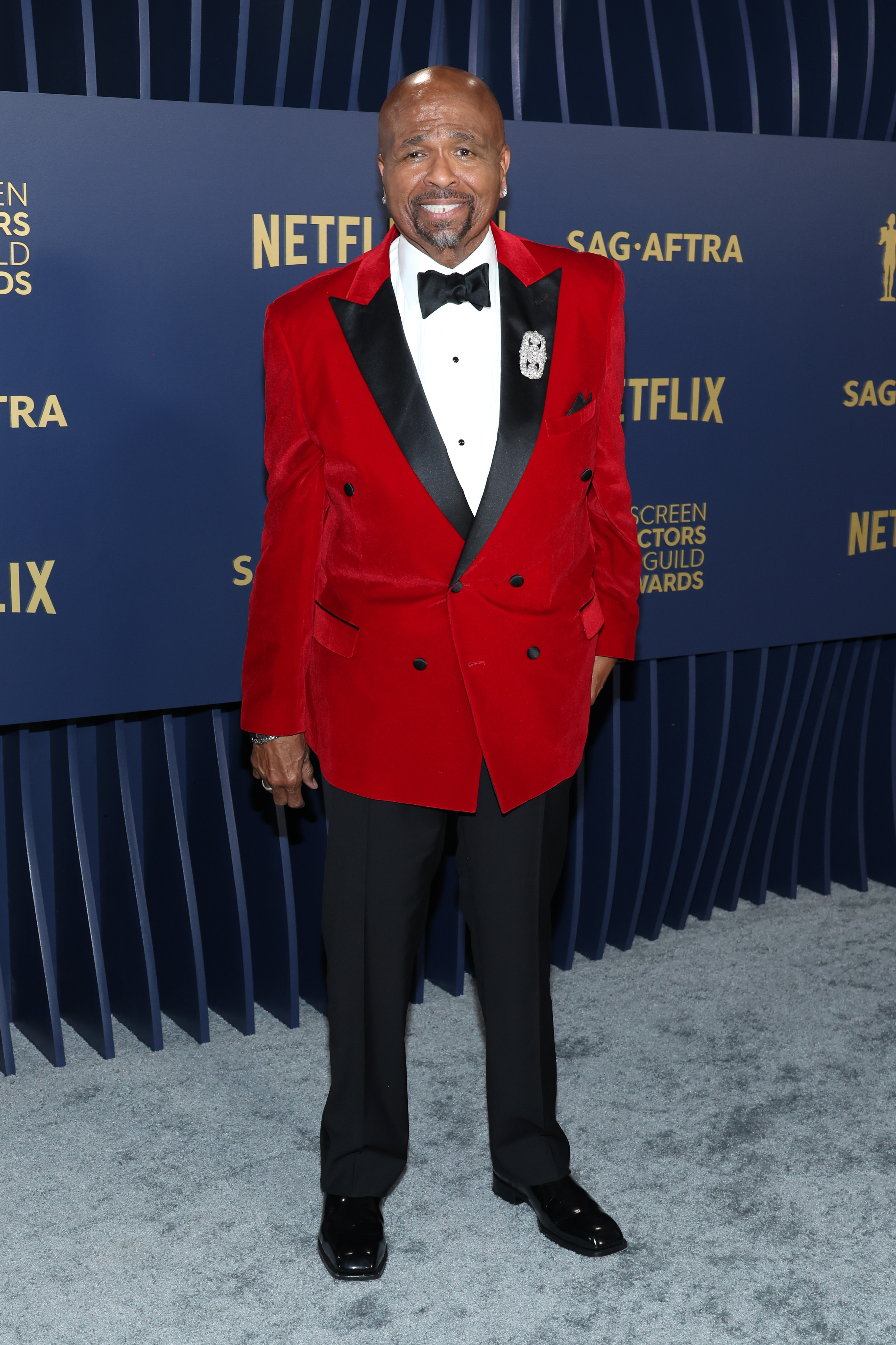 William in a red and black tuxedo with bow tie standing on event carpet