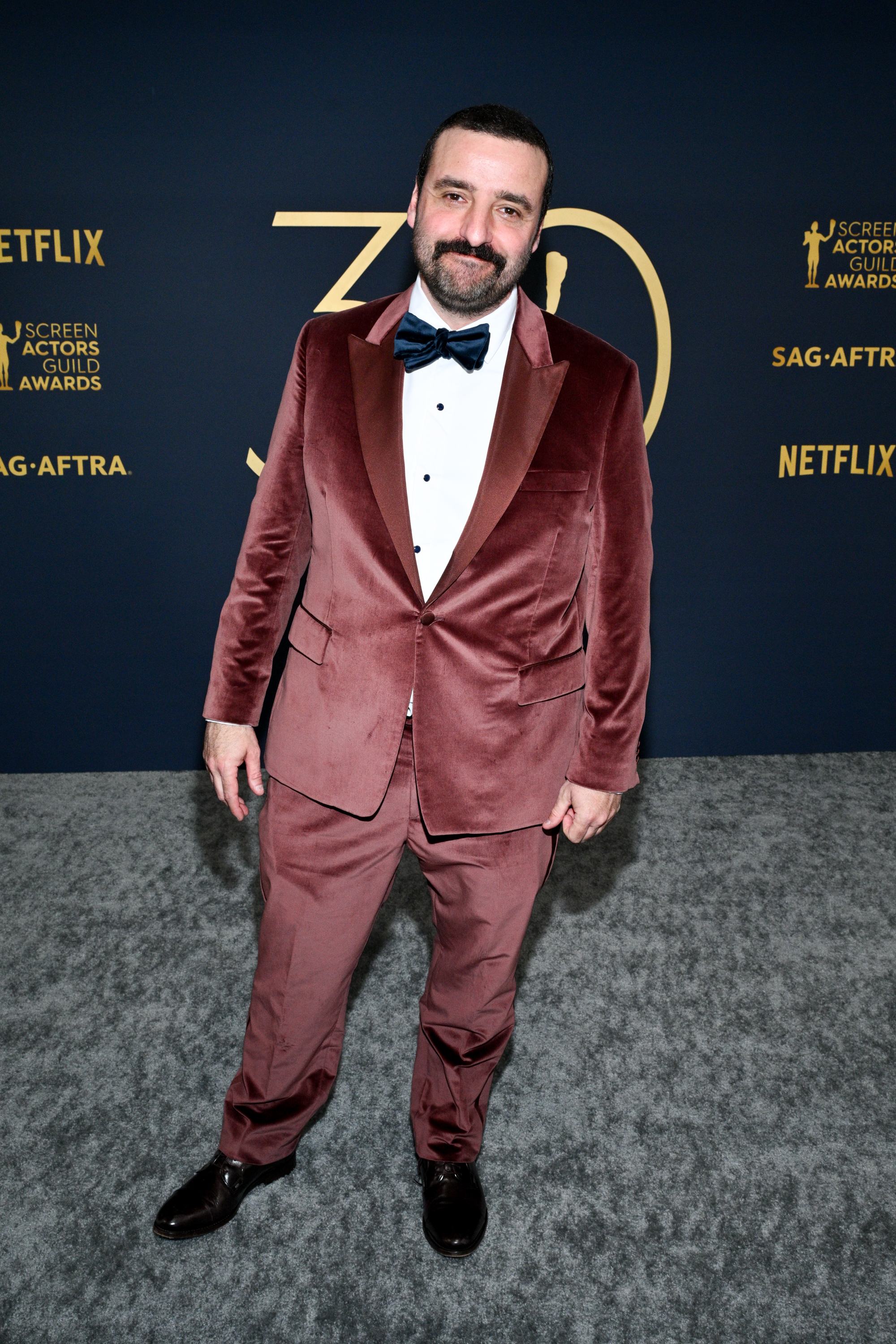 He&#x27;s in a crushed velvet suit with bow tie standing on event carpet