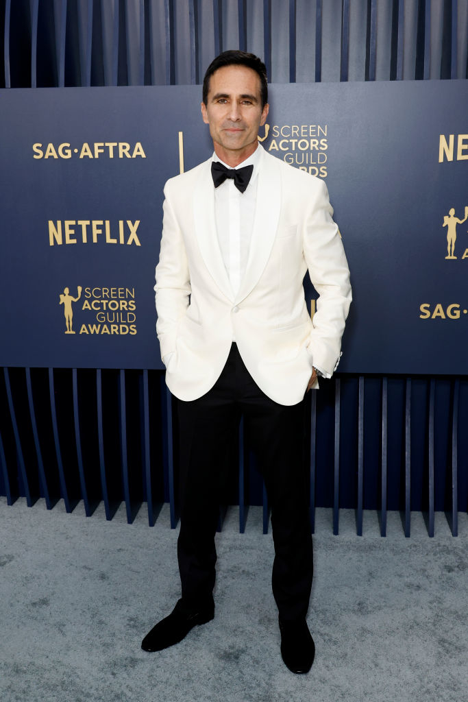 Néstor Carbonell in a white tuxedo jacket and black pants