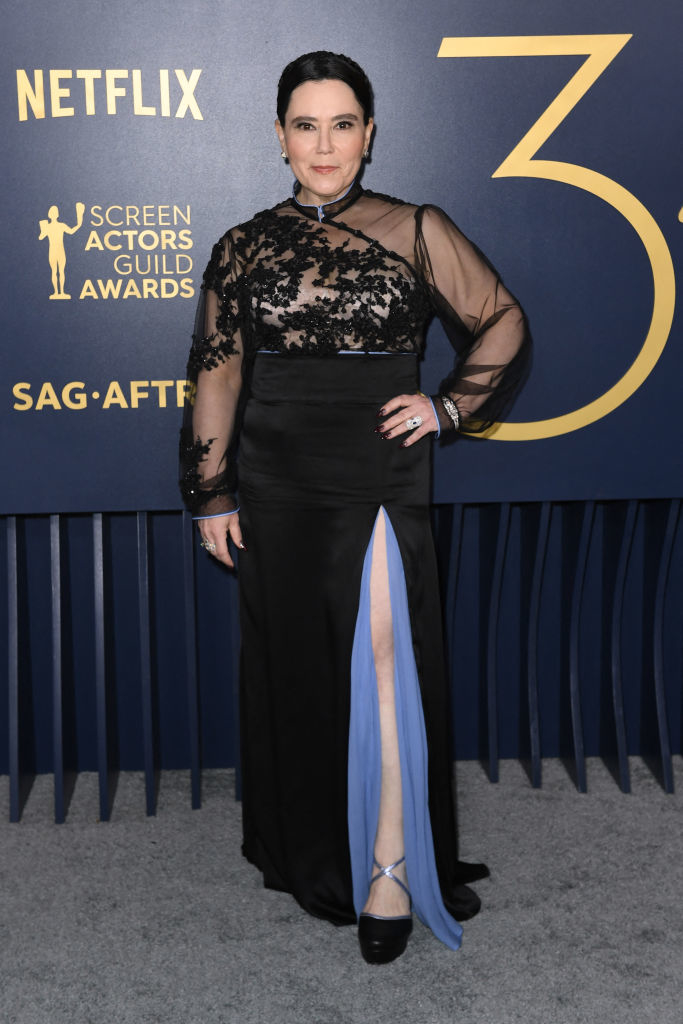 Alex Borstein in an elegant sheer-sleeved black gown with a high leg slit,