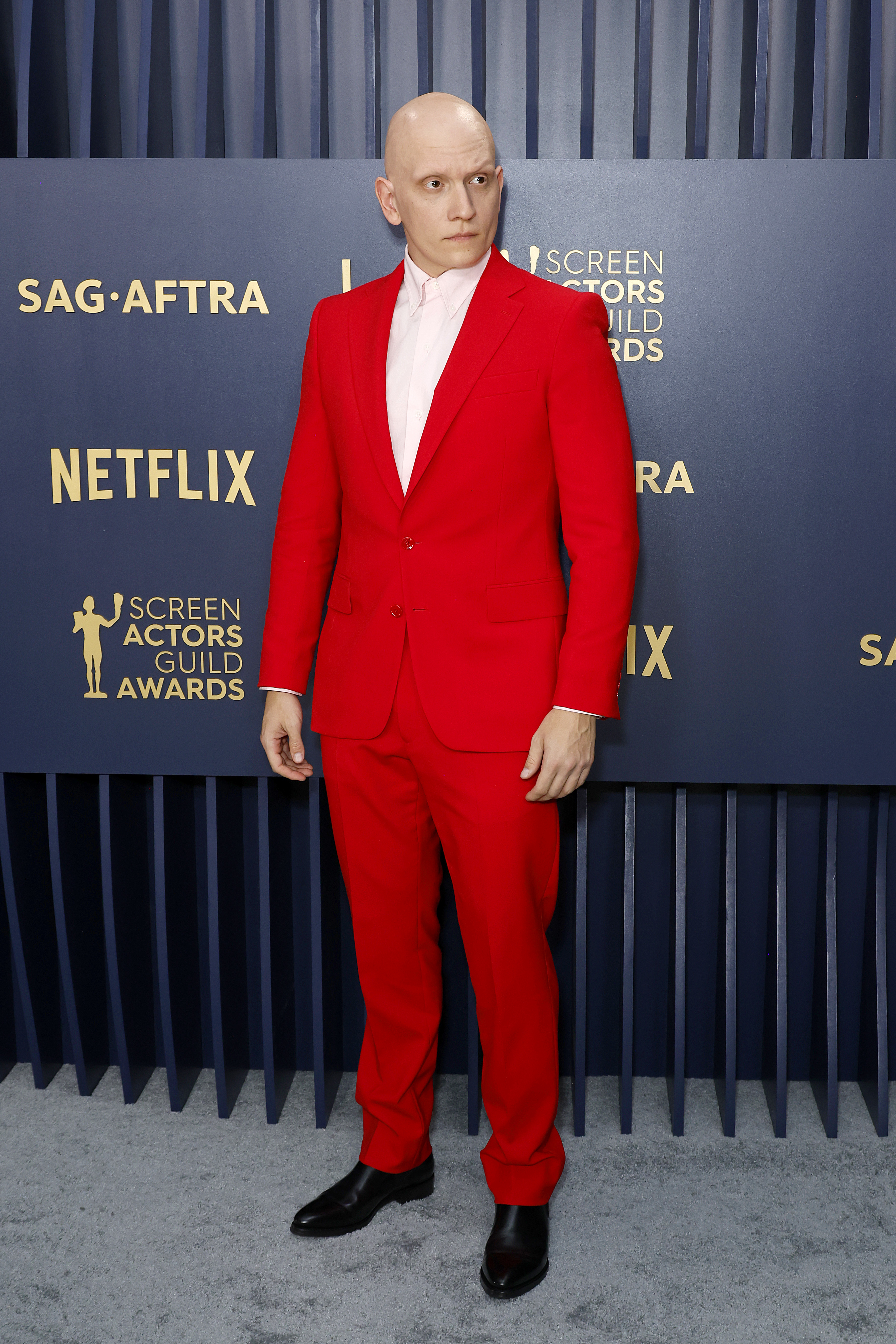 Anthony Carrigan in a sleek all-red suit and black shoes
