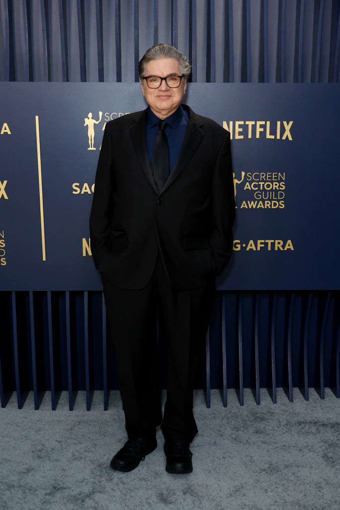 Oliver Platt in a suit and tie smiling