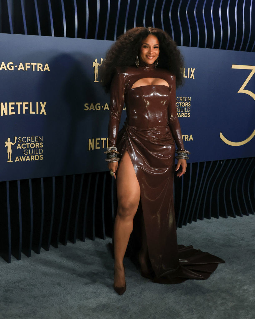 Ciara in a glossy long-sleeve leather gown with a high slit