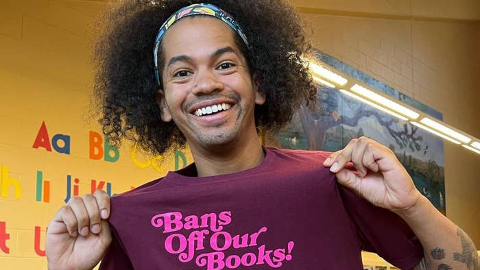 Man smiling, holding up T-shirt with &quot;Bans Off Our Books&quot; slogan, in classroom setting