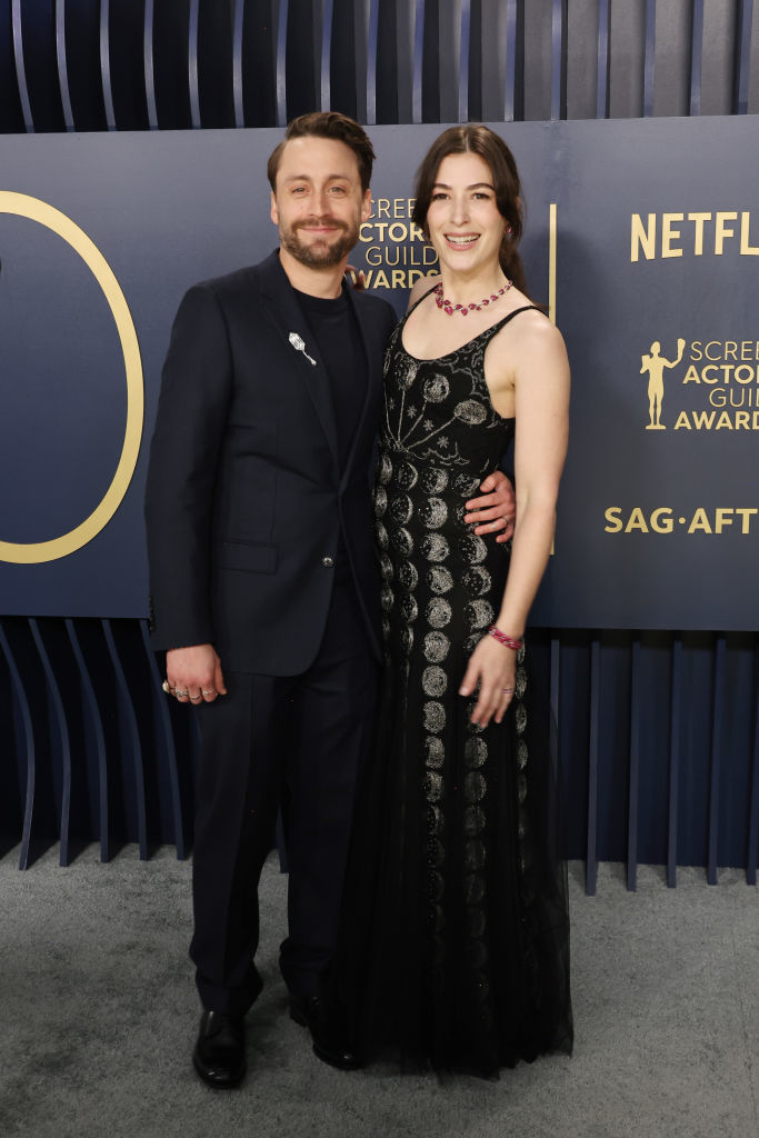 Kieran Culkin and Jazz Charton standing together; one in a black suit, the other in a black embroidered gown with jewelry