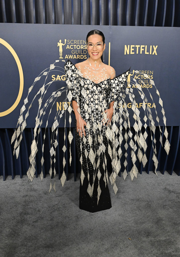 Ali Wong  in a unique black and white gown with an intricate pattern and extended, fringed sleeves stands smiling