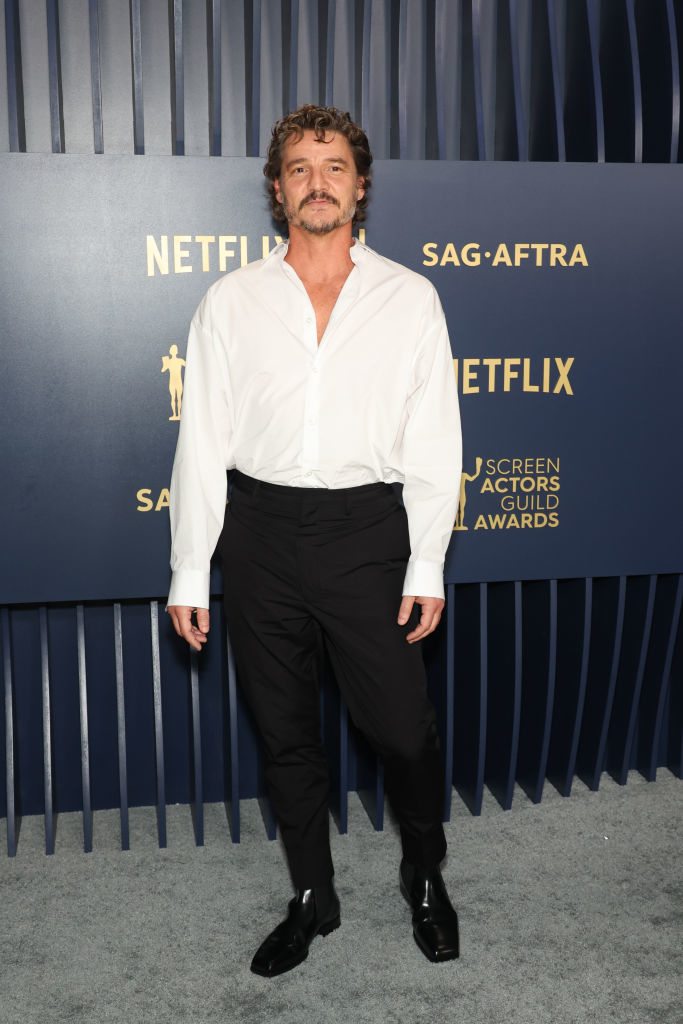Pedro Pascal in a semi-formal attire with an unbuttoned white shirt and black trousers at an event