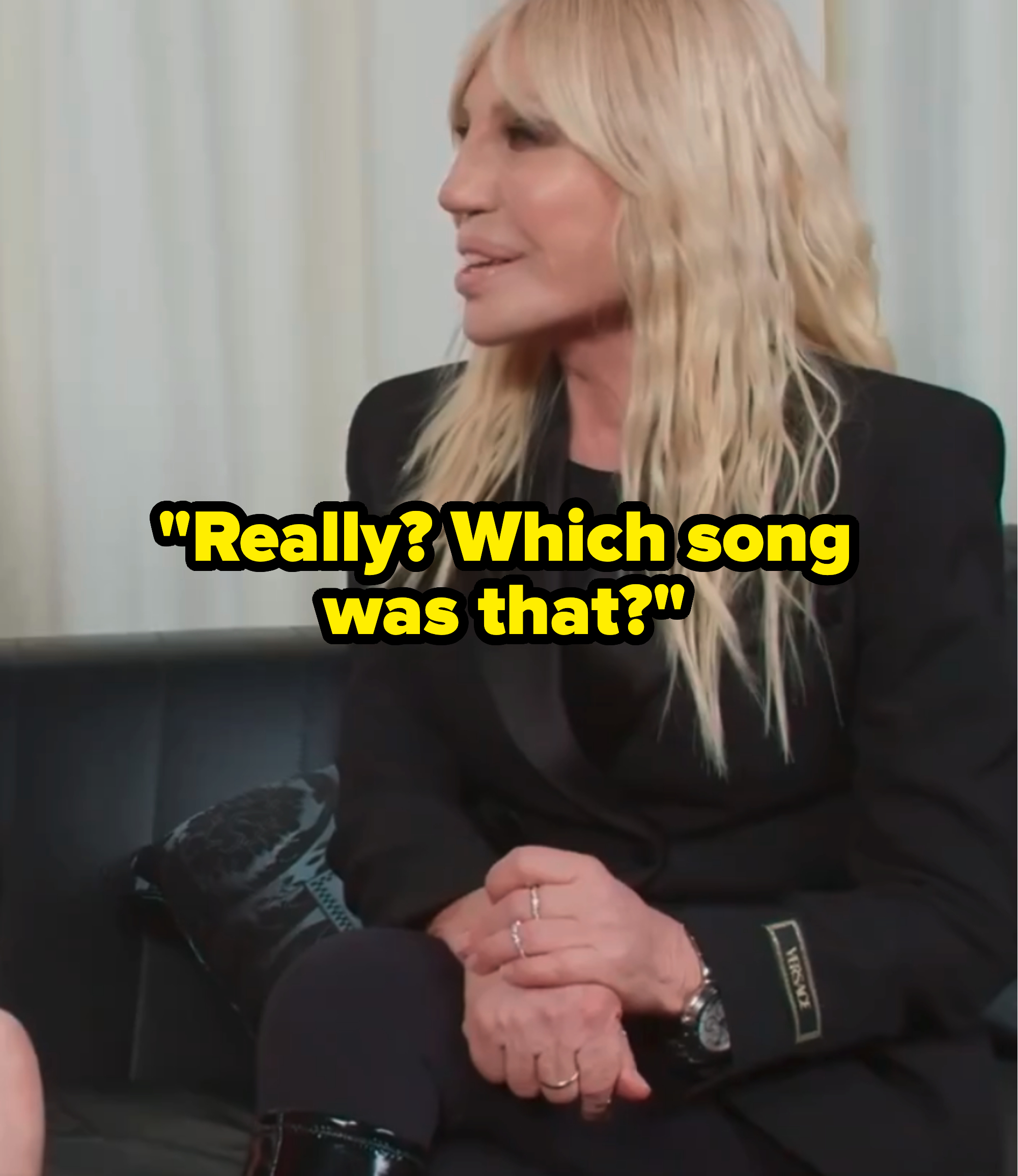 Donatella Versace wearing a black blazer, seated and engaged in conversation