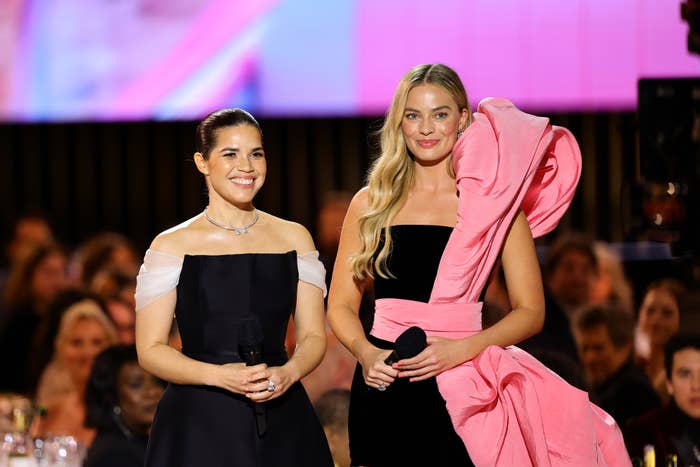A closeup of america ferrera and margot robbie on stage hoiding mics