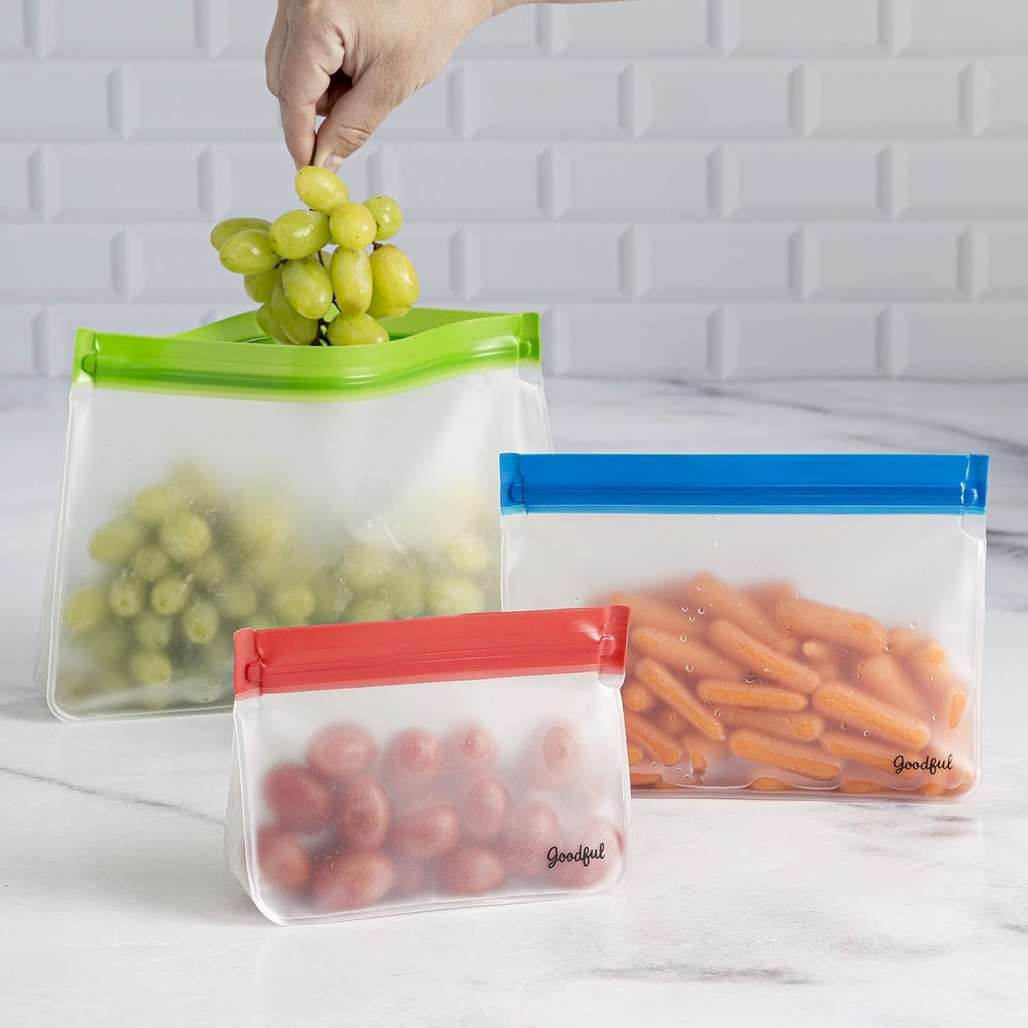 Hand placing grapes into an open reusable storage bag with two more filled bags beside it