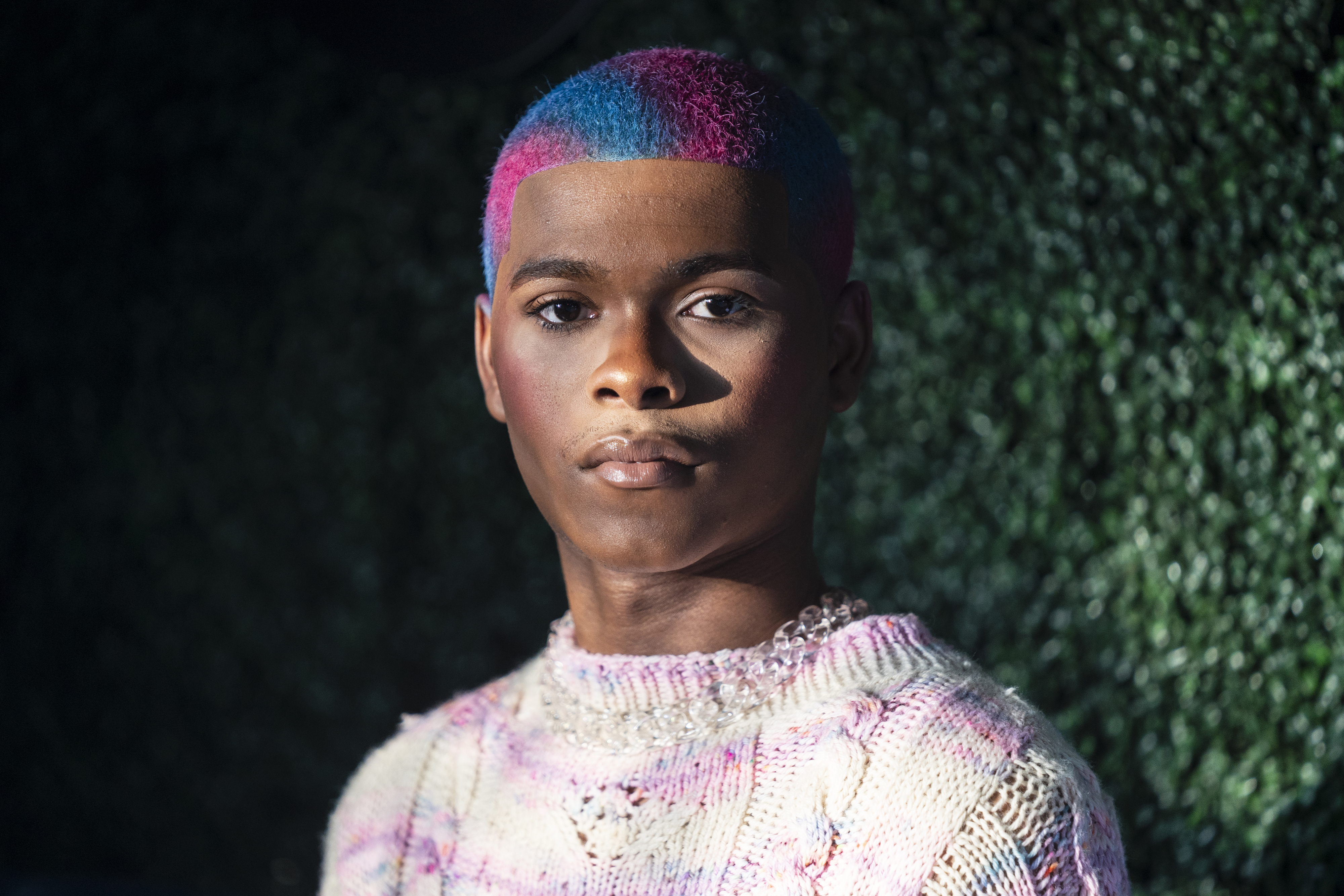 Kidd Kenn with a multicolored hair design and a textured sweater posing for the camera
