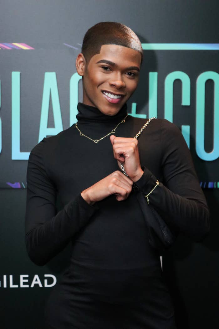 Kidd Kenn posing with hands clasped, wearing a high-neck outfit and a chain necklace