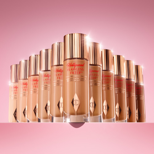 Array of Charlotte Tilbury&#x27;s Hollywood Flawless Filter makeup bottles against a pink background