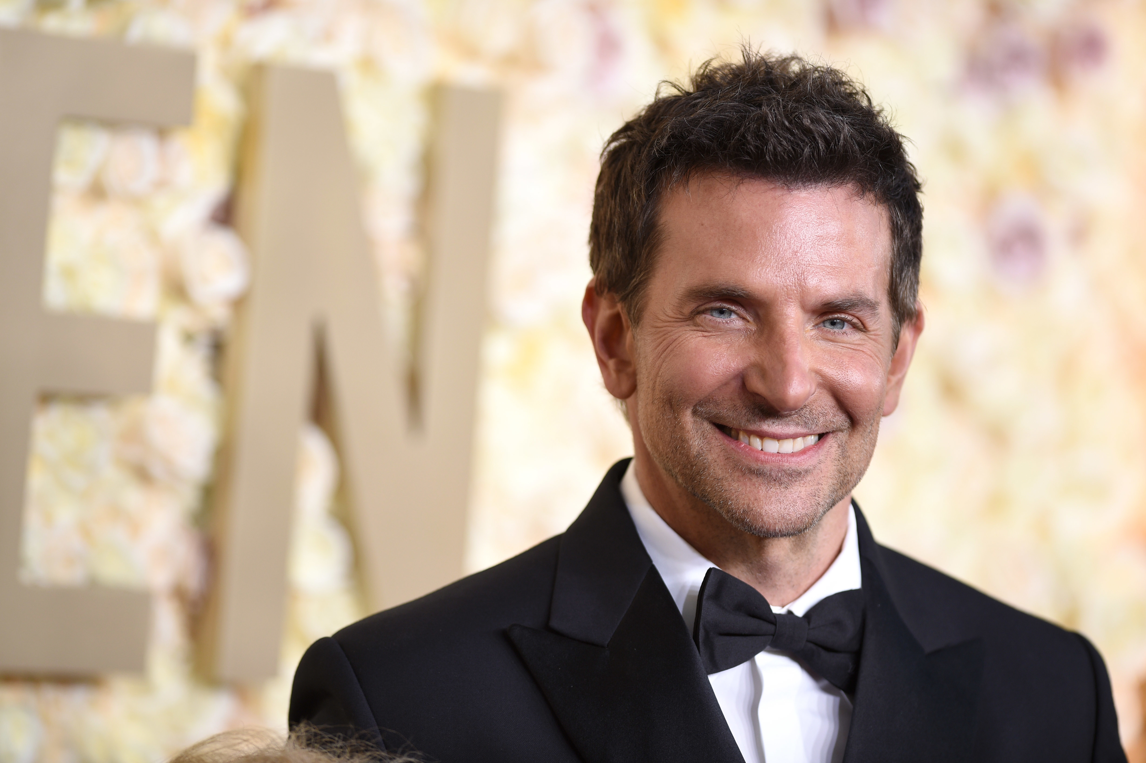 Bradley Cooper in a tuxedo on a red carpet smiling