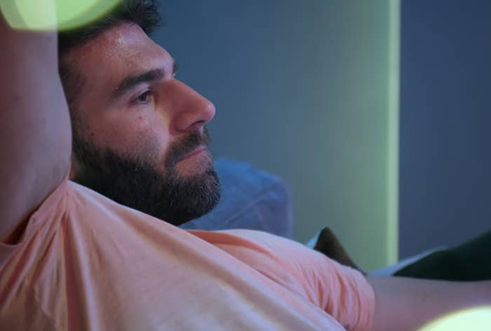 Man lounging on a sofa, watching television, with ambient lighting in the background