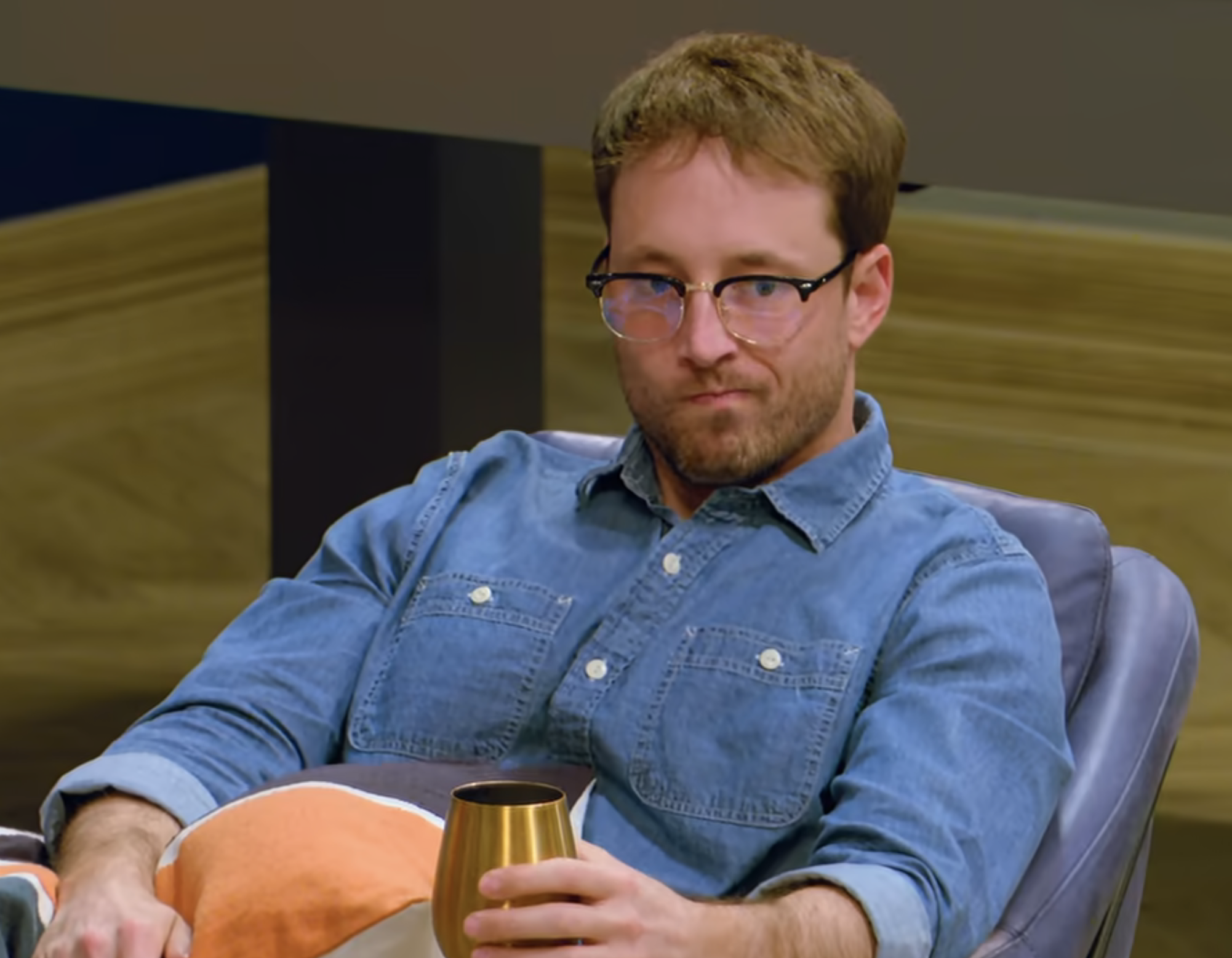 Jeramey Lutinski  in a denim shirt sitting with a cup, looking toward camera, with a screen in the background