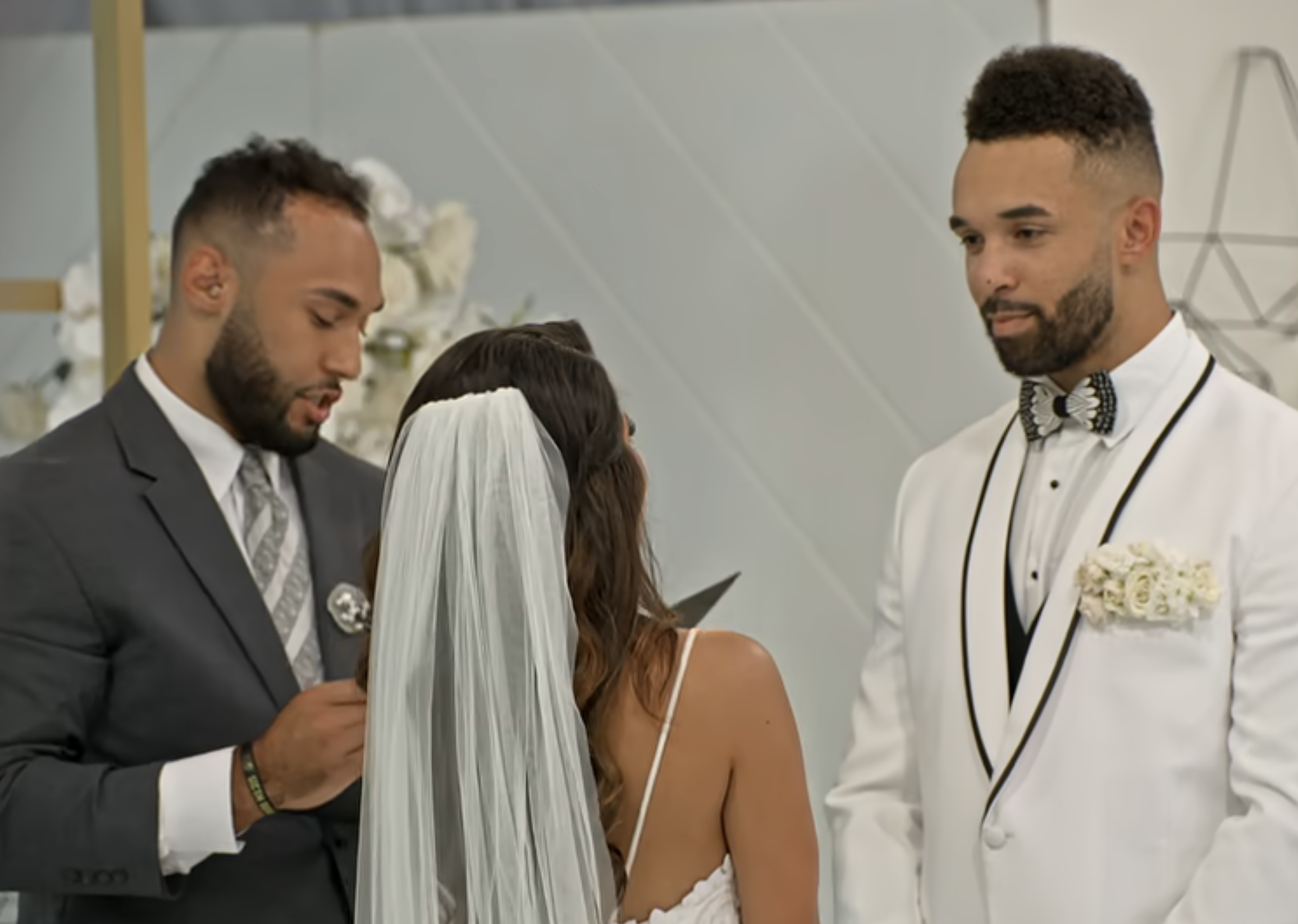 Two men in formal attire with a bride during a wedding ceremony. One is adjusting the other's attire