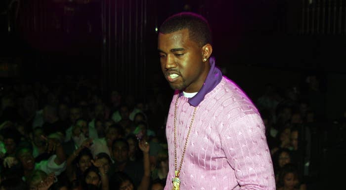 Kanye West in a textured purple shirt and gold chain performing on stage