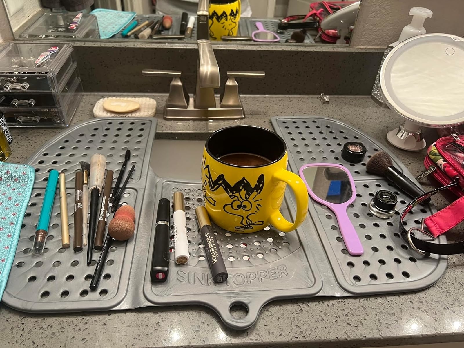 A bathroom counter with various makeup items and a mug featuring a cartoon character, surrounded by beauty accessories
