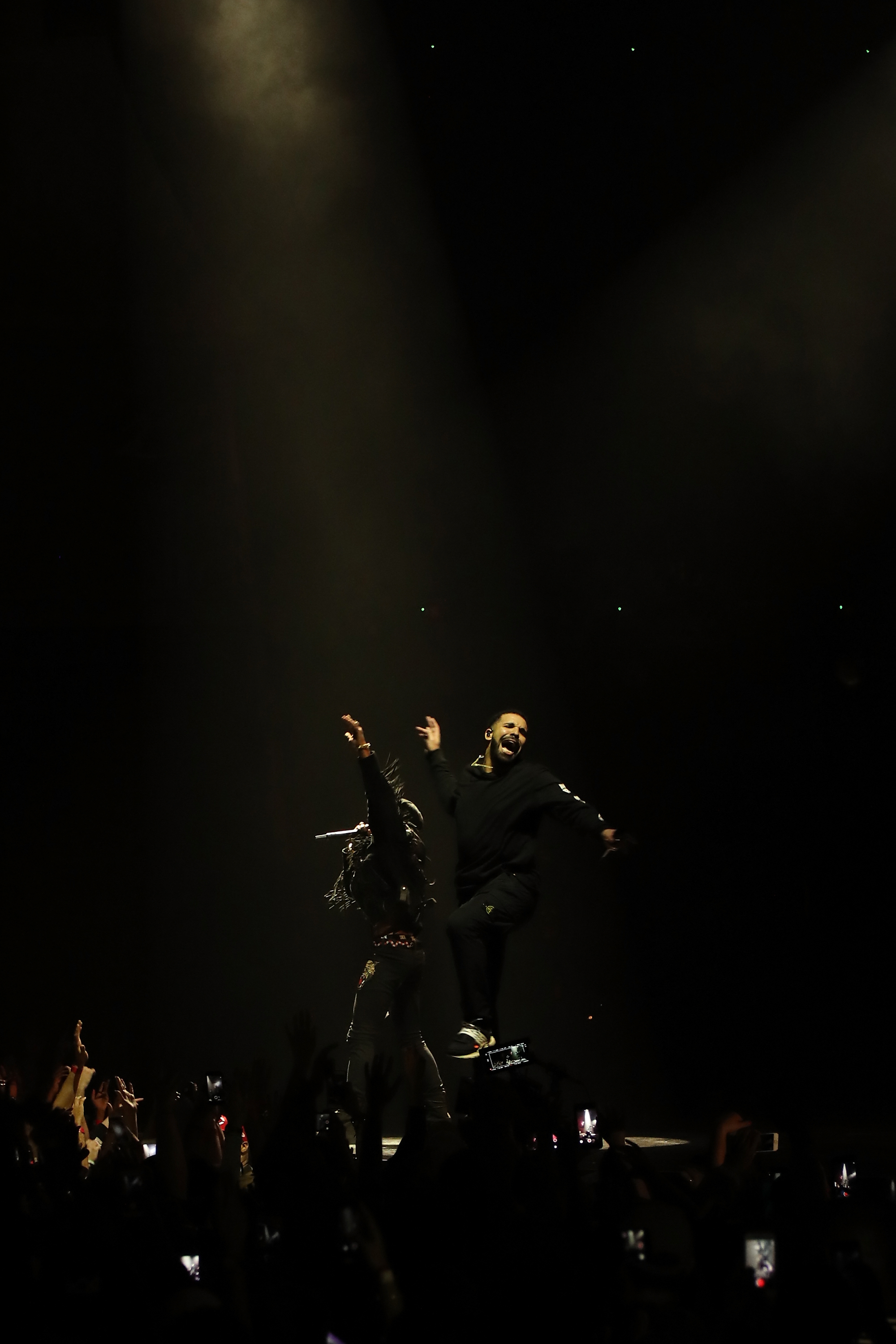 Drake performing onstage in a spotlight with an audience in the foreground