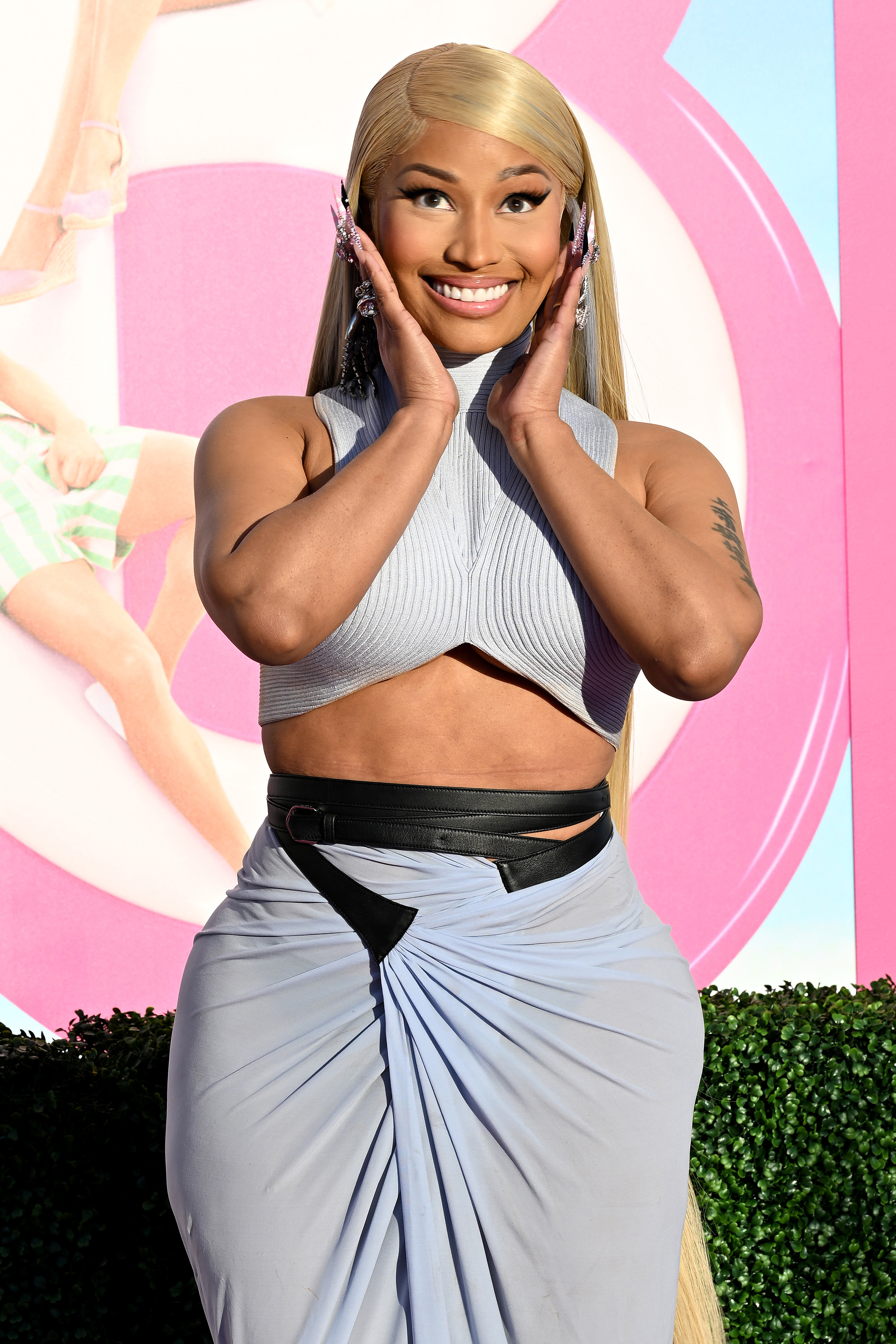 Nicki Minaj in a cropped top and high-waisted skirt, hands framing face, smiling