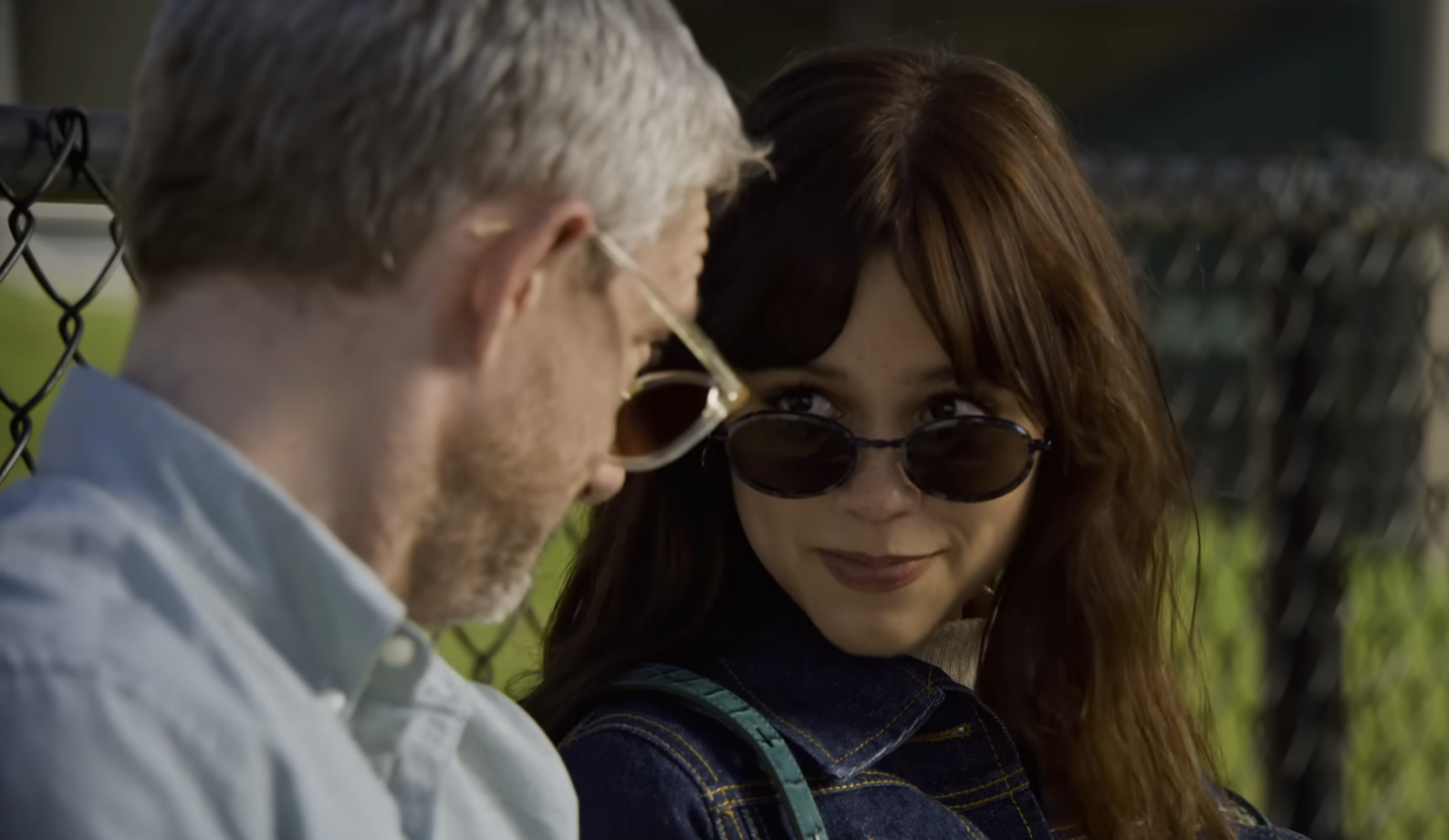 Jenna and Martin in casual wear sitting close looking over their sunglasses at each other