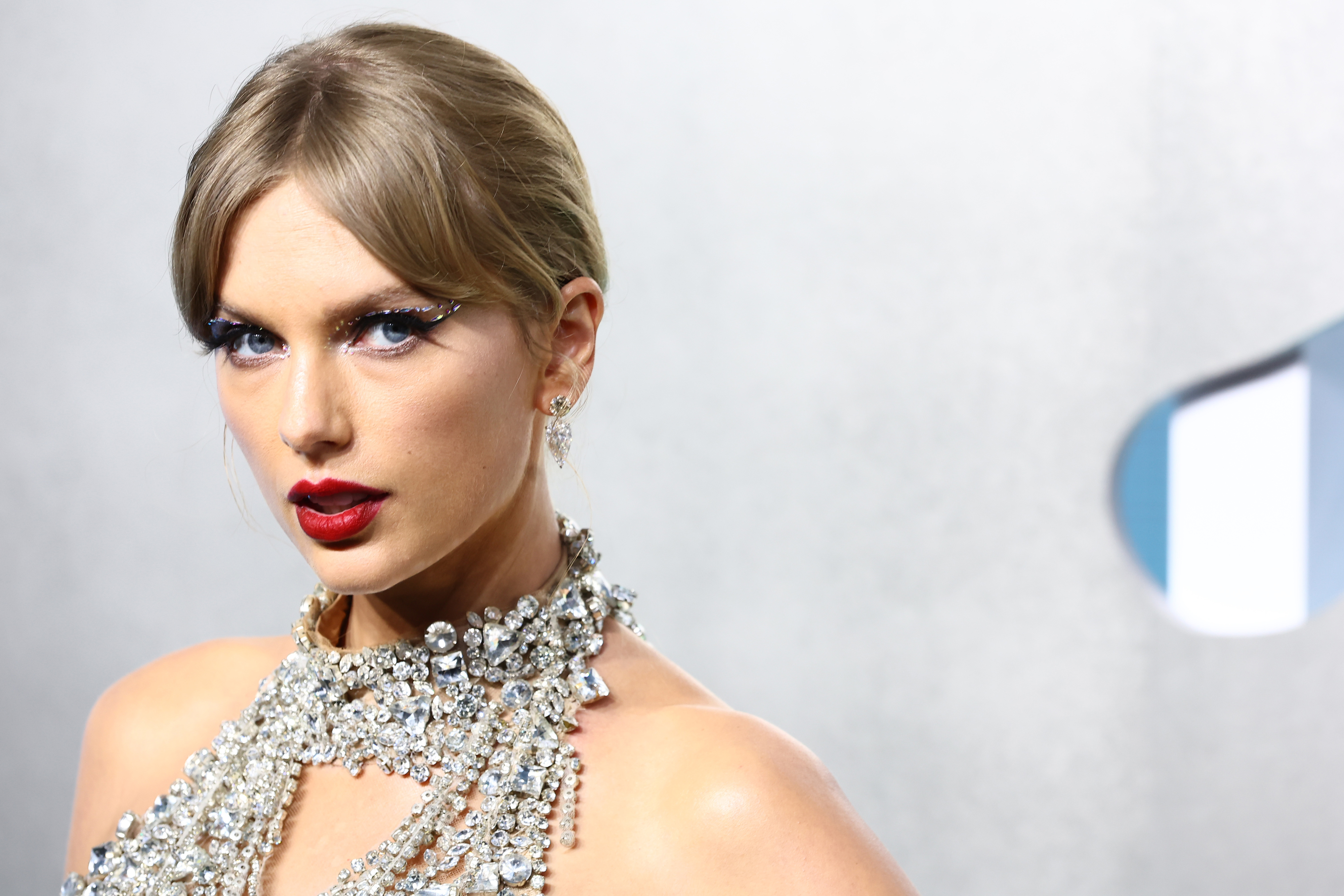 Taylor Swift wearing a sparkling bejeweled necklace and dramatic makeup, posing at an event