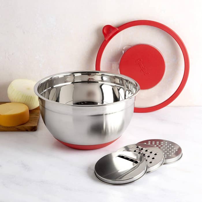 stainless steel mixing bowl with a red silicone lid and interlocking grater attachments on a kitchen counter
