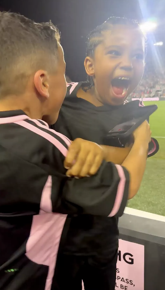 Two children, one cheering excitedly, hugging at a sporting event