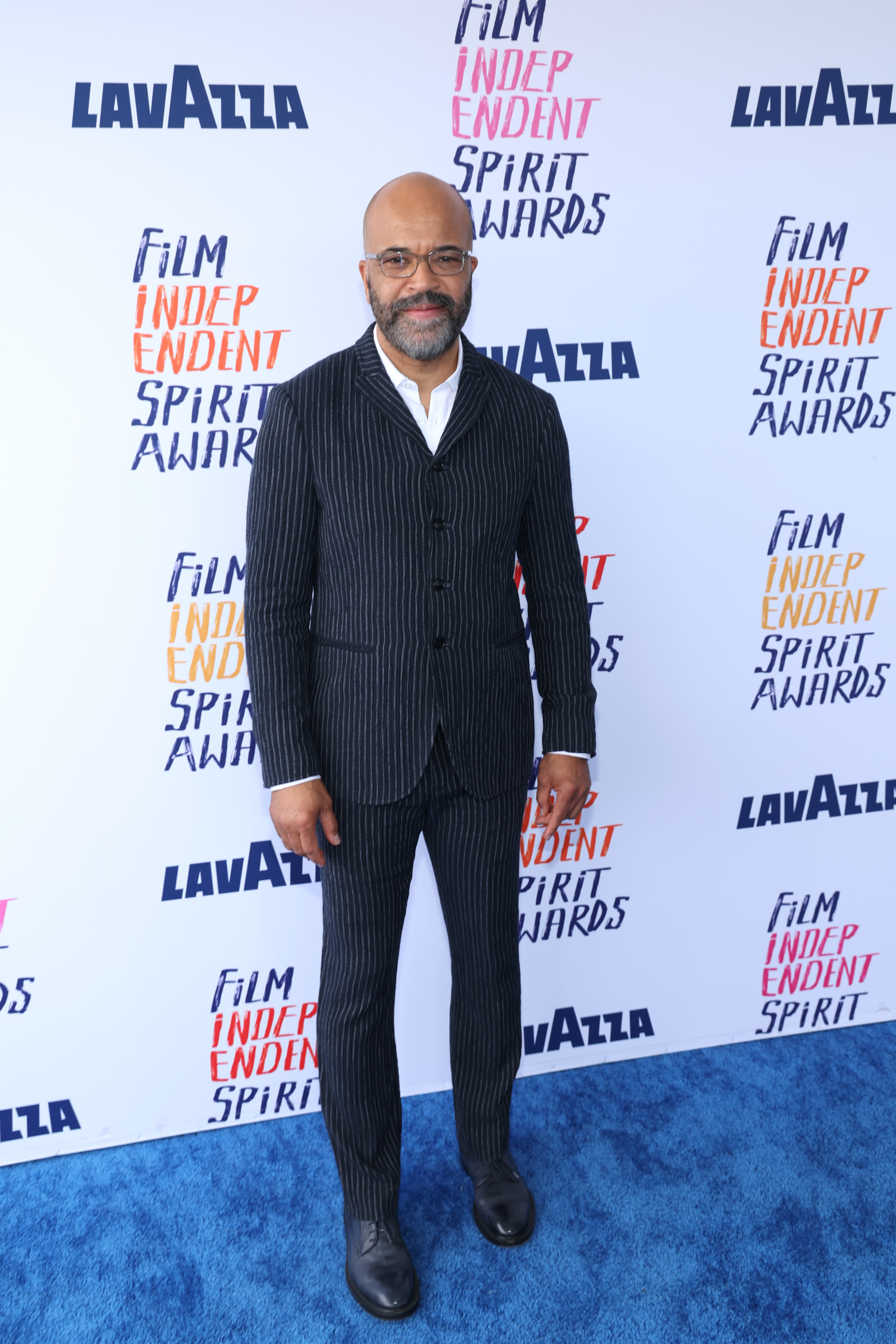 Jeffrey Wright wearing a striped suit with a buttoned-up shirt and glasses