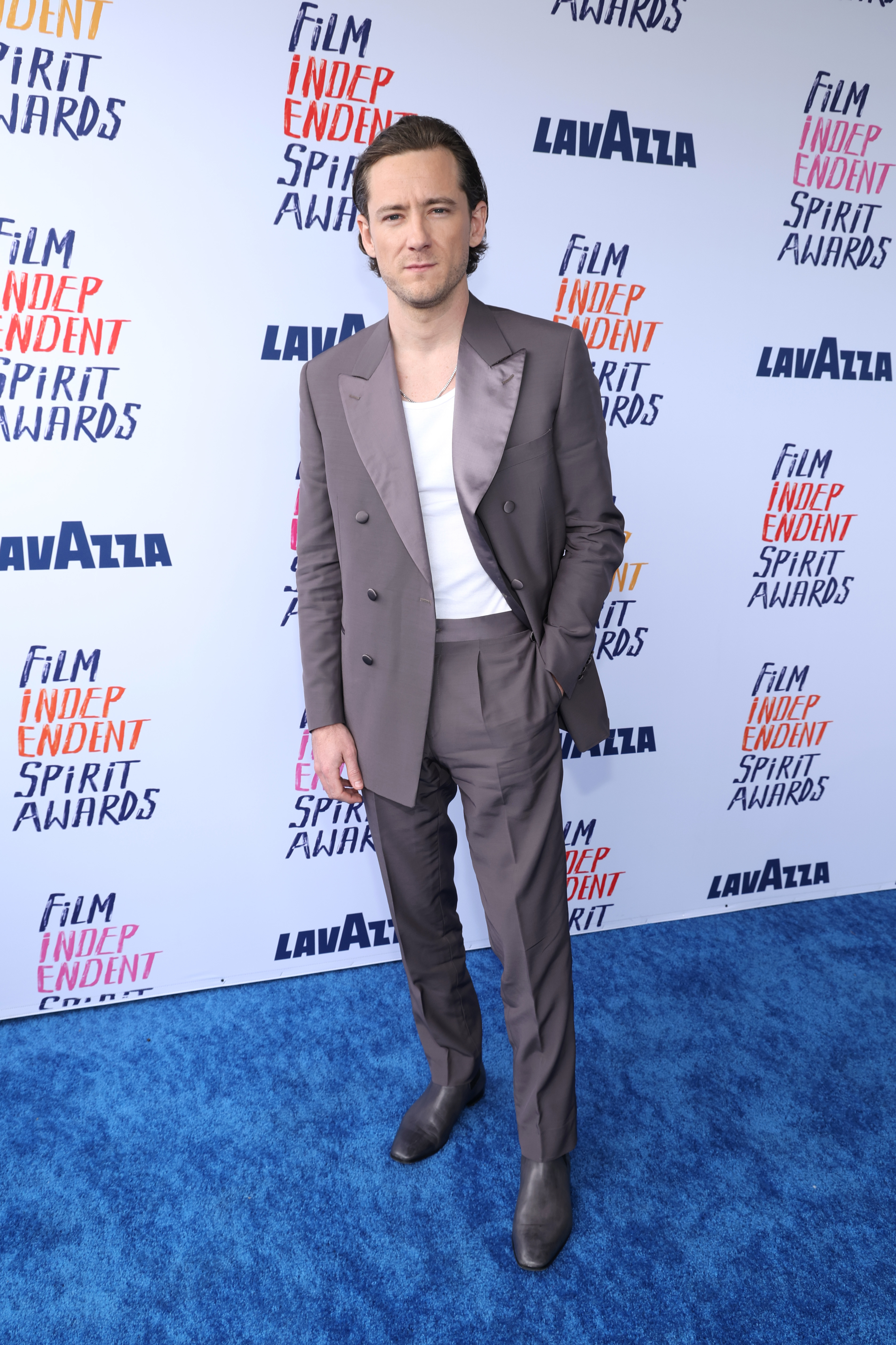 Lewis  wearing a blazer over an open-collar shirt, paired with tailored trousers and boots