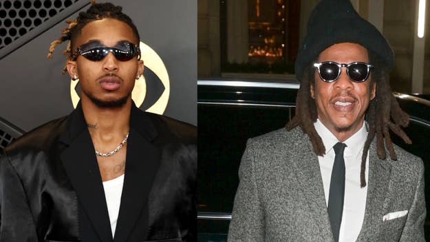 Two male musicians, one in a black tuxedo with a necklace, the other in a tweed jacket and hat, both wearing sunglasses