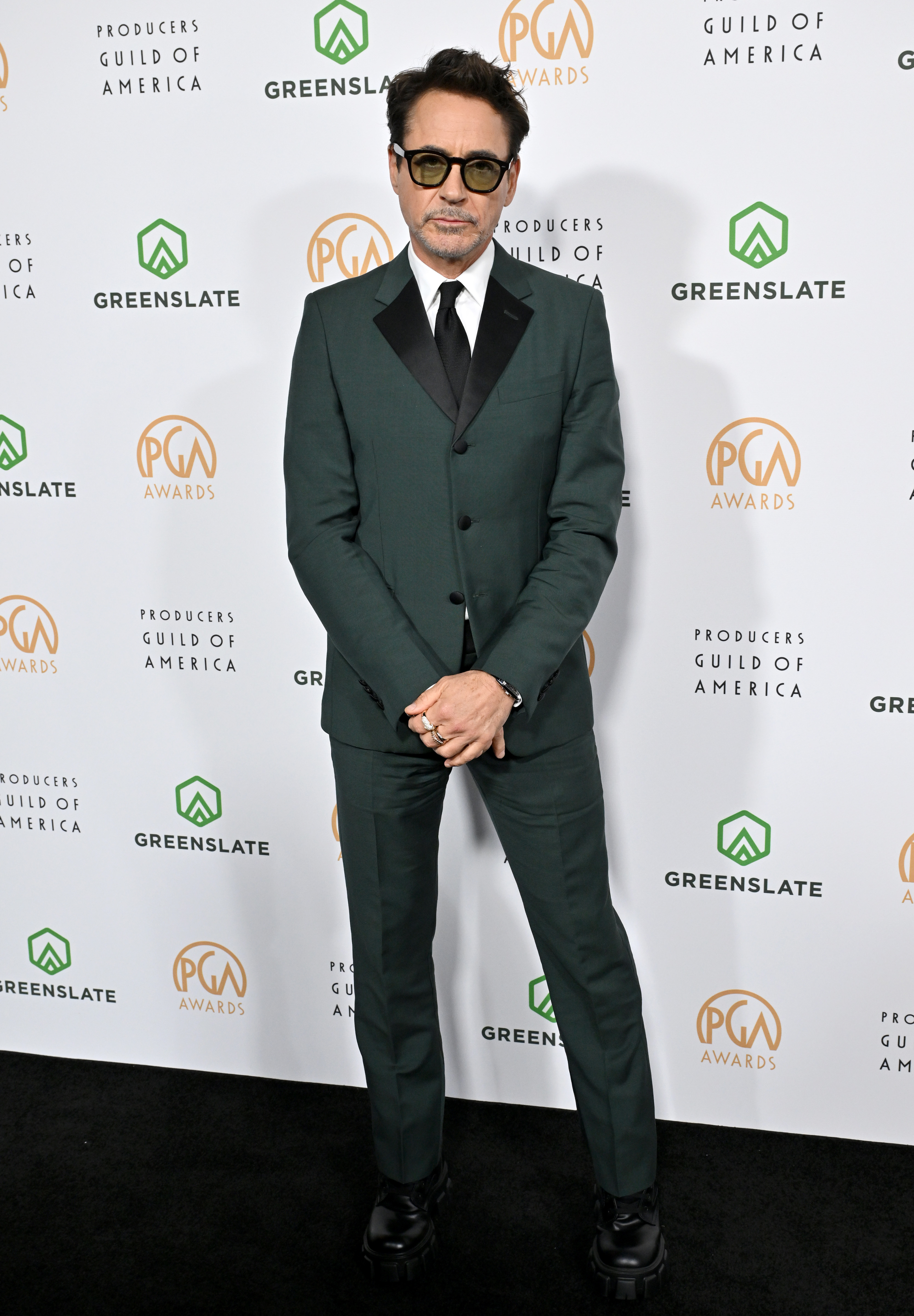 Robert Downey Jr. stands in front of a Producers Guild of America backdrop wearing a sharp suit