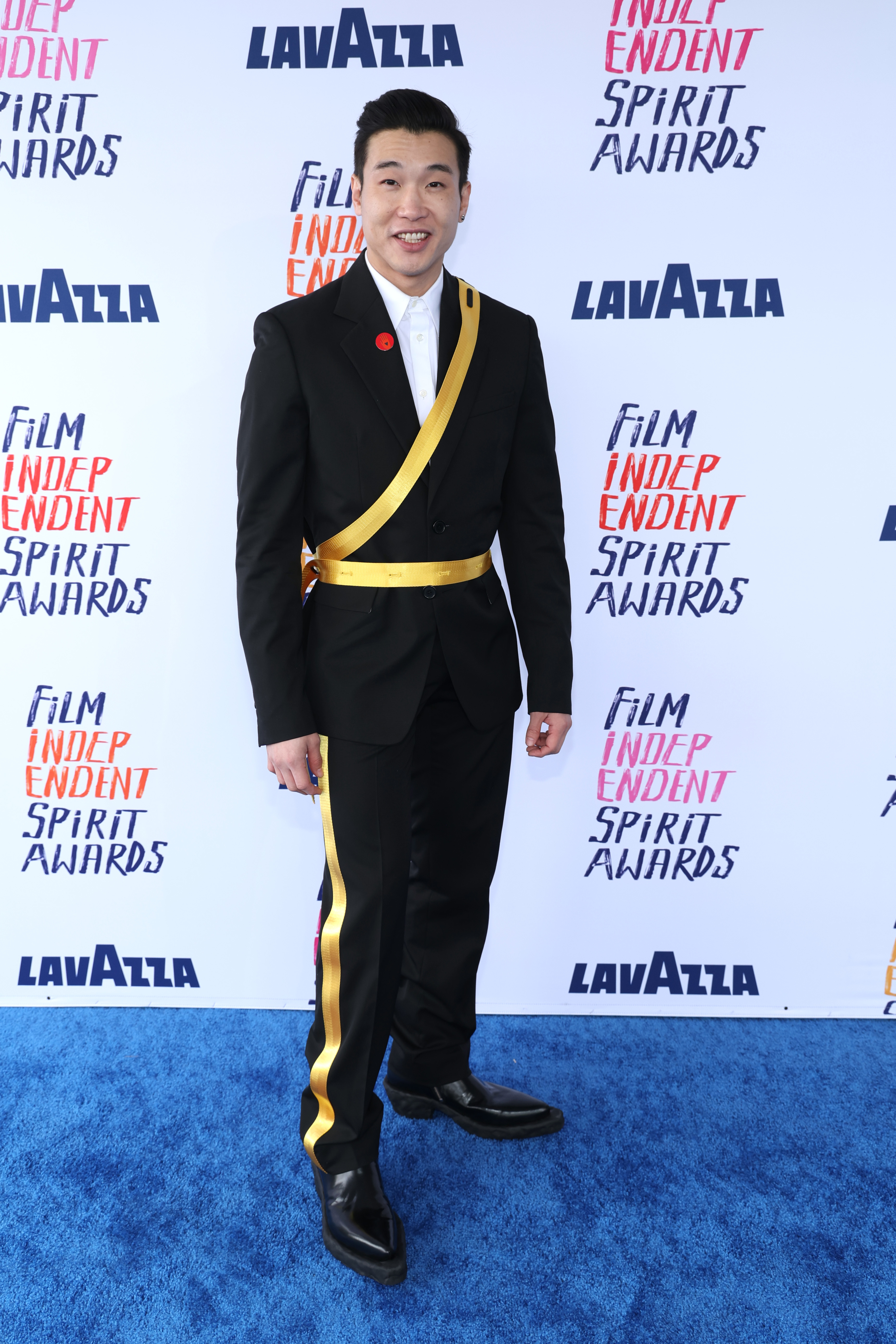 Joel in unique black suit with stripes across the chest and down the pant legs posing at Film Independent Spirit Awards