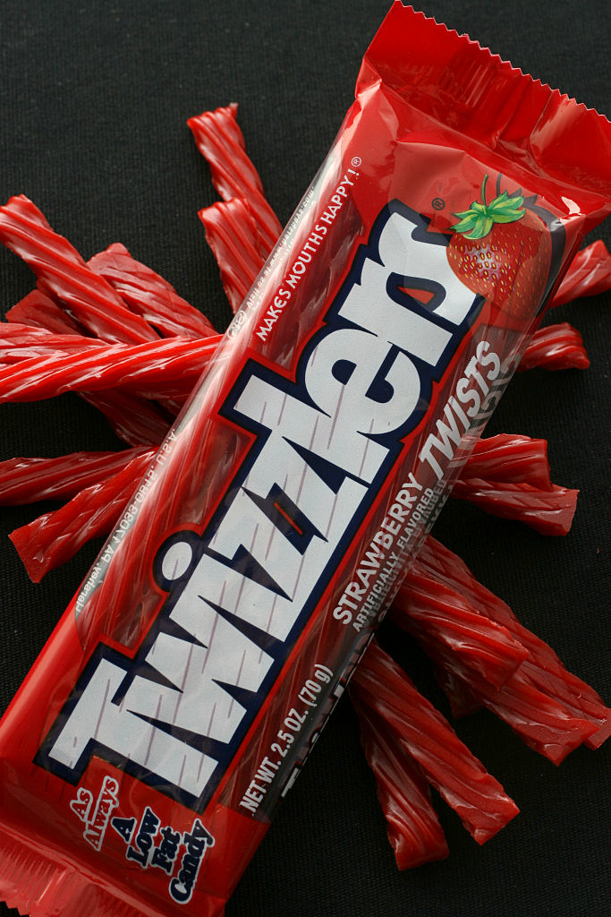 A pack of Twizzlers Strawberry Twists lies atop scattered individual candies