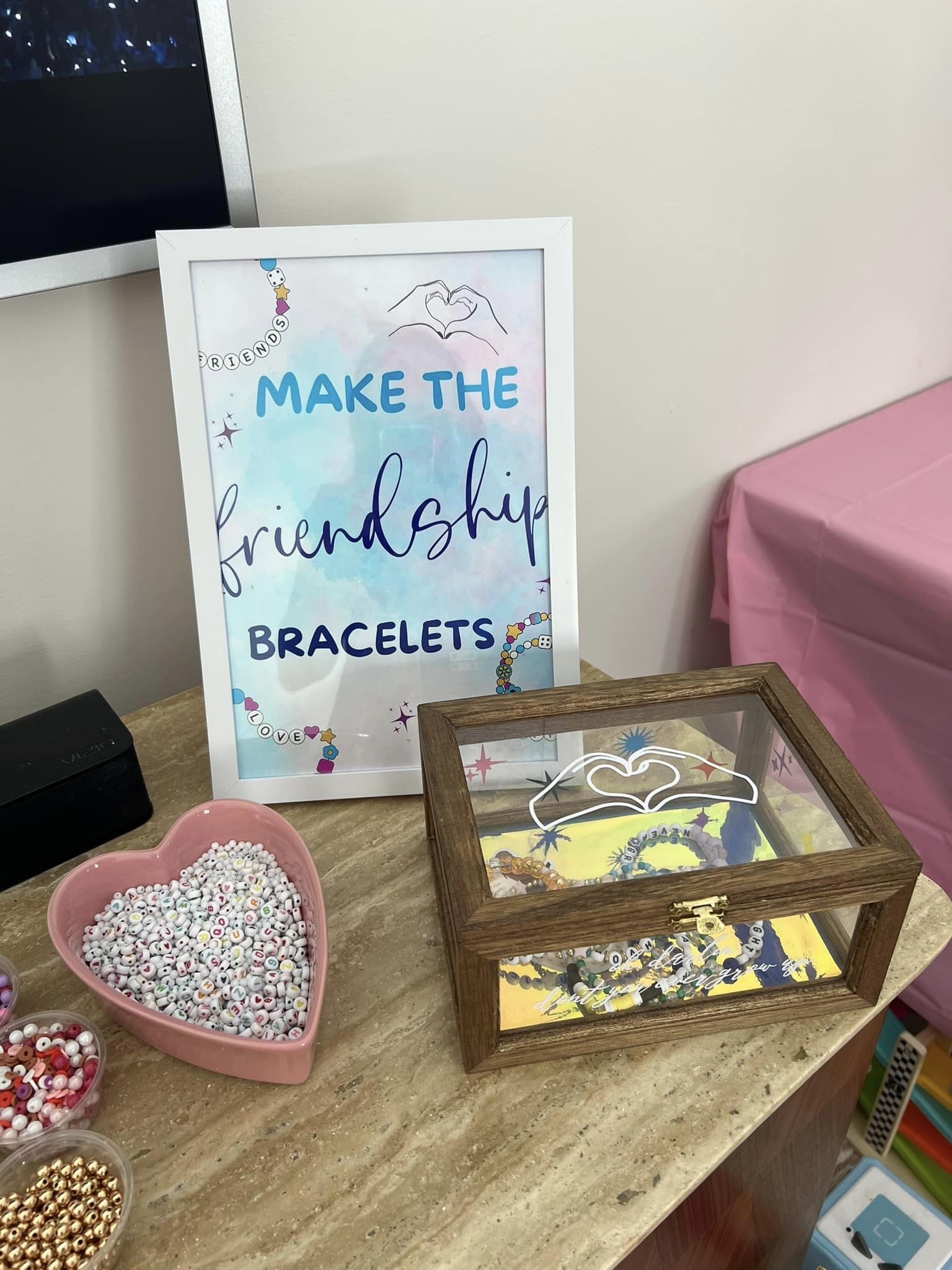 Crafting supplies and a sign that says &quot;MAKE THE friendship BRACELETS&quot; on a table with beads and strings for bracelet making