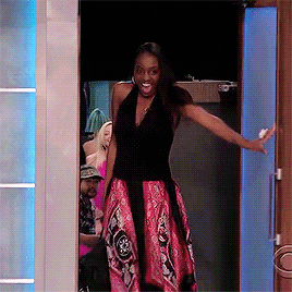 A meme of woman in sleeveless top and patterned skirt entering a room, arms wide with a joyful expression